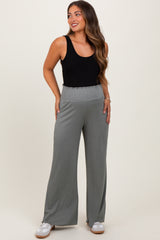 woman wearing a black tank top and light gray wide-leg maternity pants, showing a baby bump