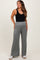 woman wearing a black tank top and light gray wide-leg maternity pants, showing a baby bump