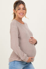 woman wearing a light brown waffle knit maternity sweater and holding her baby bump