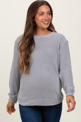 woman wearing a light grey maternity sweater with long sleeves and a relaxed fit, smiling while showcasing her baby bump