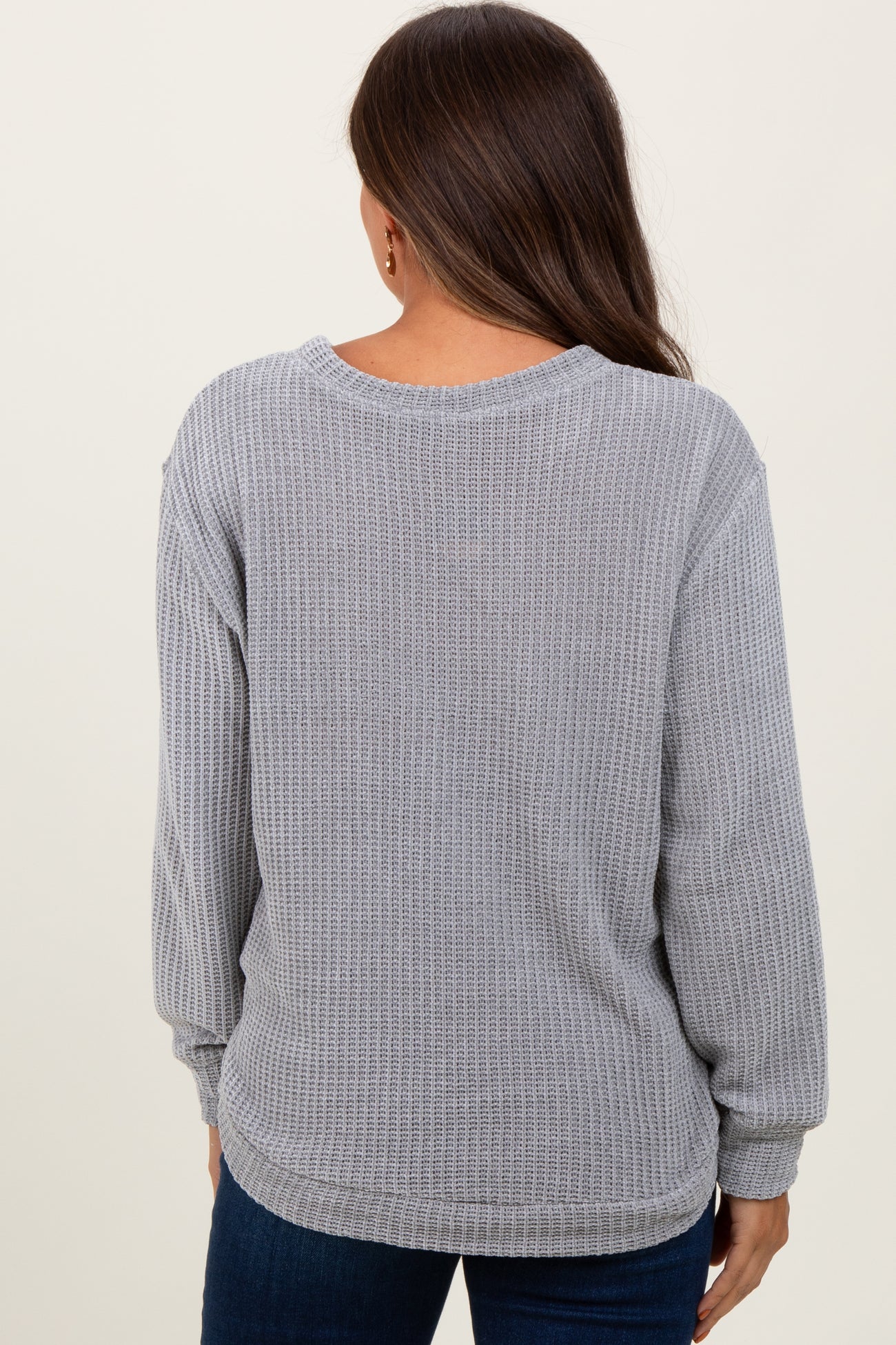 woman wearing a gray long sleeve maternity waffle knit top, showing the back view and styled with blue jeans