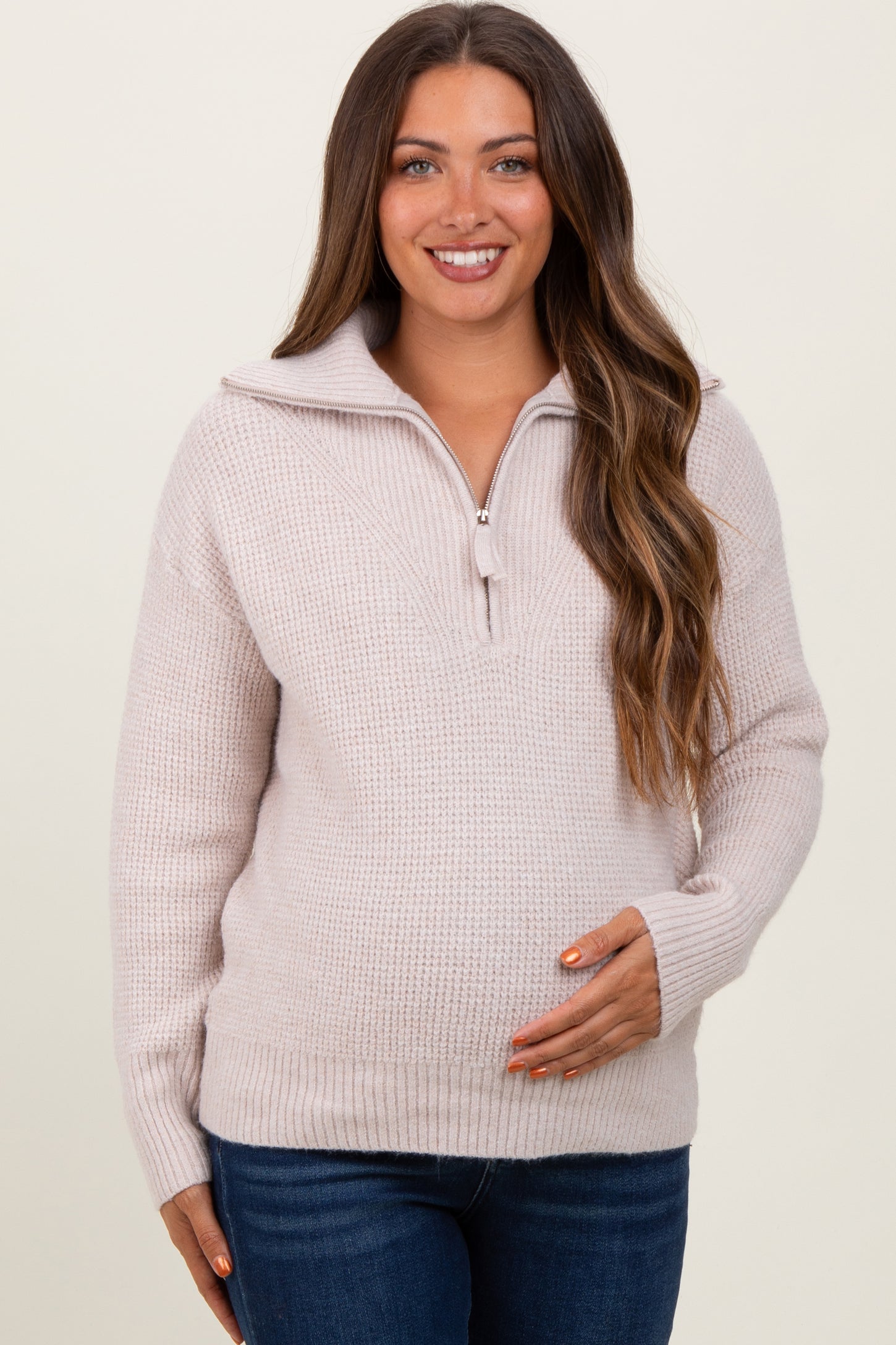 woman wearing a light pink maternity sweater with a quarter-zip and holding her baby bump