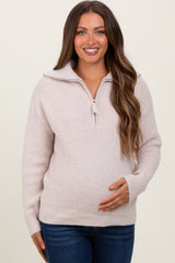 woman wearing a light pink maternity sweater with a quarter-zip and holding her baby bump