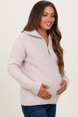 woman wearing a light pink zip-up maternity sweater and holding her baby bump