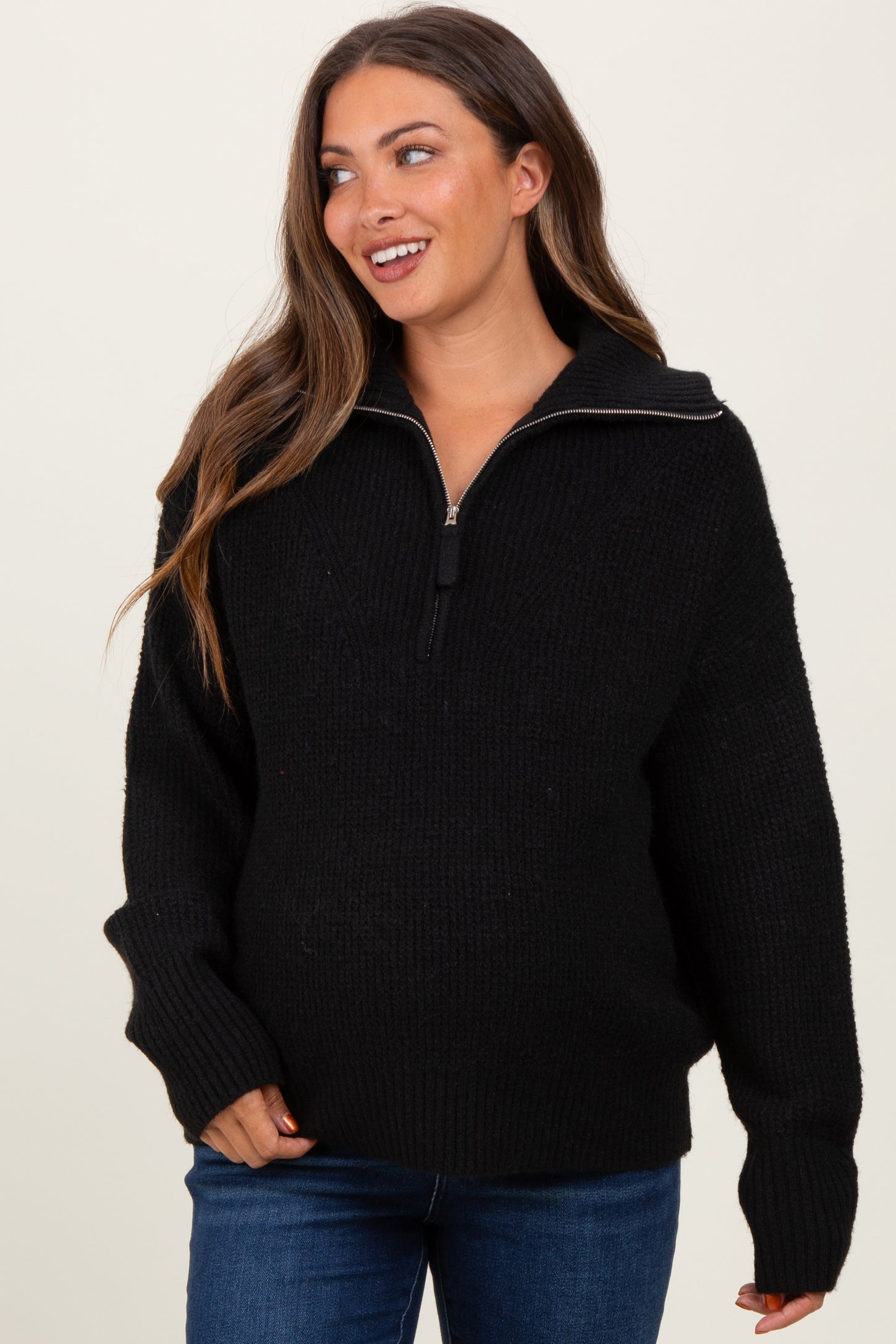 woman wearing a black maternity pullover sweater with half-zip and oversized fit, showcasing her baby bump
