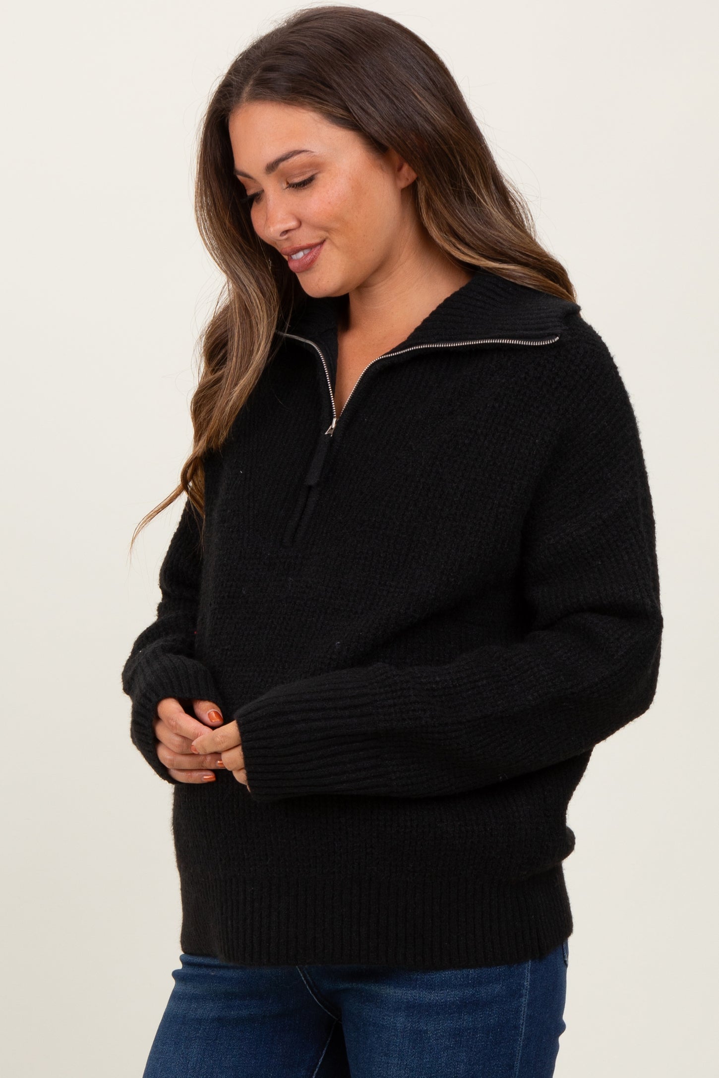 woman wearing a black maternity sweater with a half-zip collar and relaxed fit, cradling her baby bump