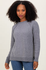 woman wearing a grey knit sweater with a ribbed hem and side slits, paired with blue jeans