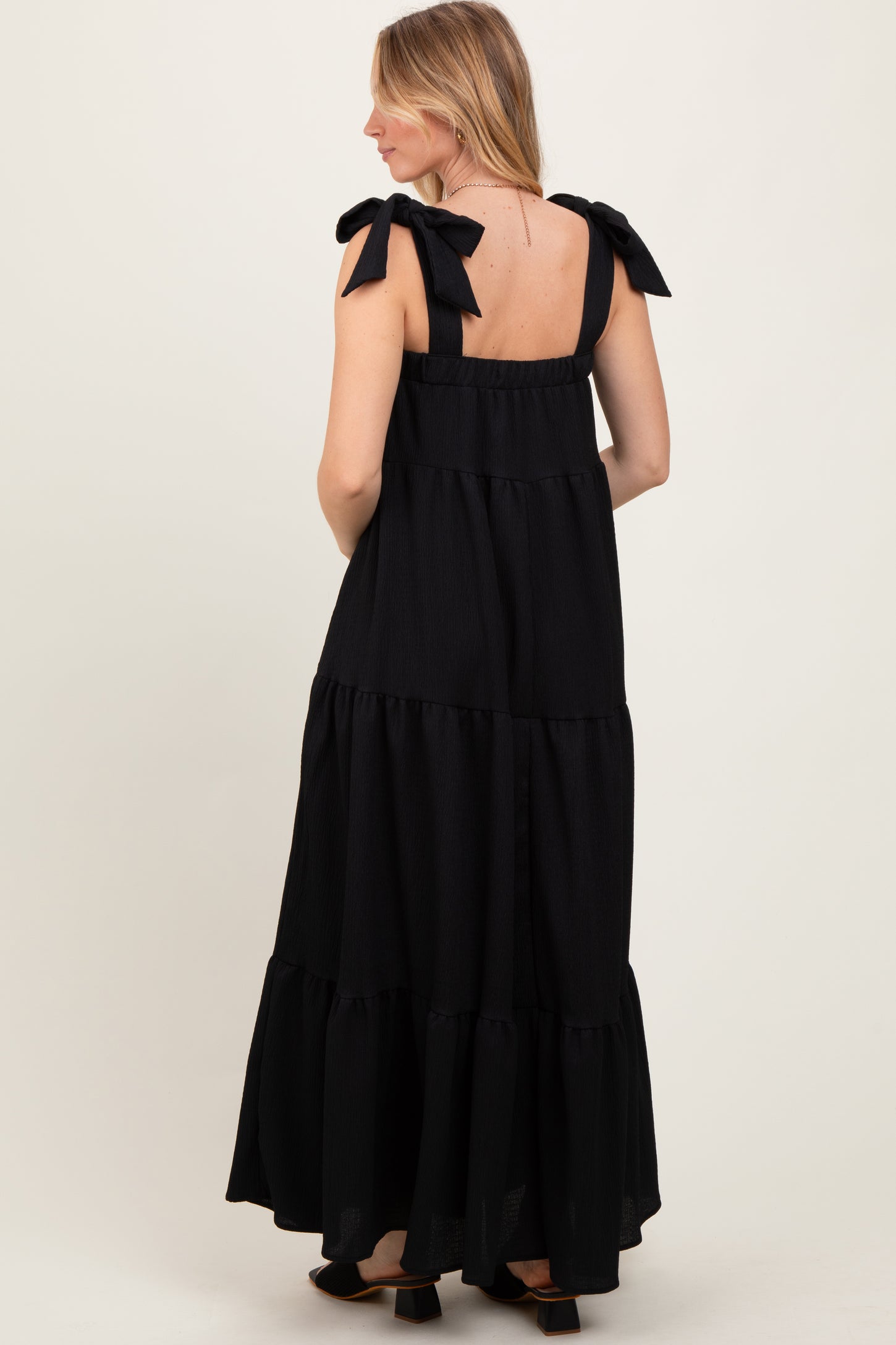 woman wearing a black tiered maxi dress with bow tie straps and a flowy silhouette, viewed from the back