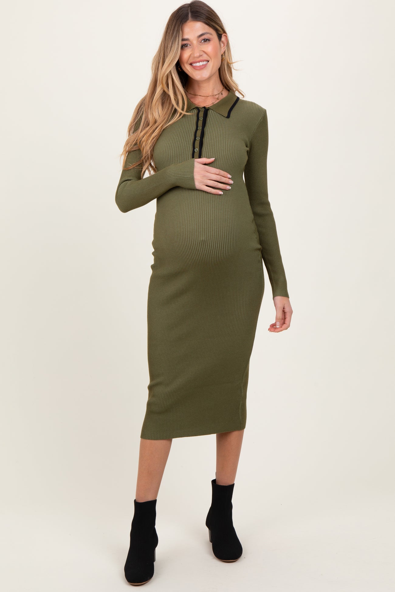 woman wearing a green ribbed maternity dress with long sleeves and a front button detail, holding her baby bump