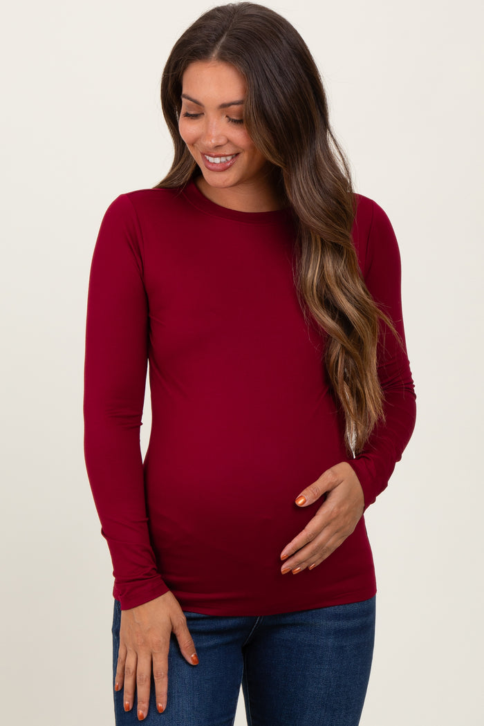 woman wearing a burgundy long sleeve maternity top and holding her baby bump