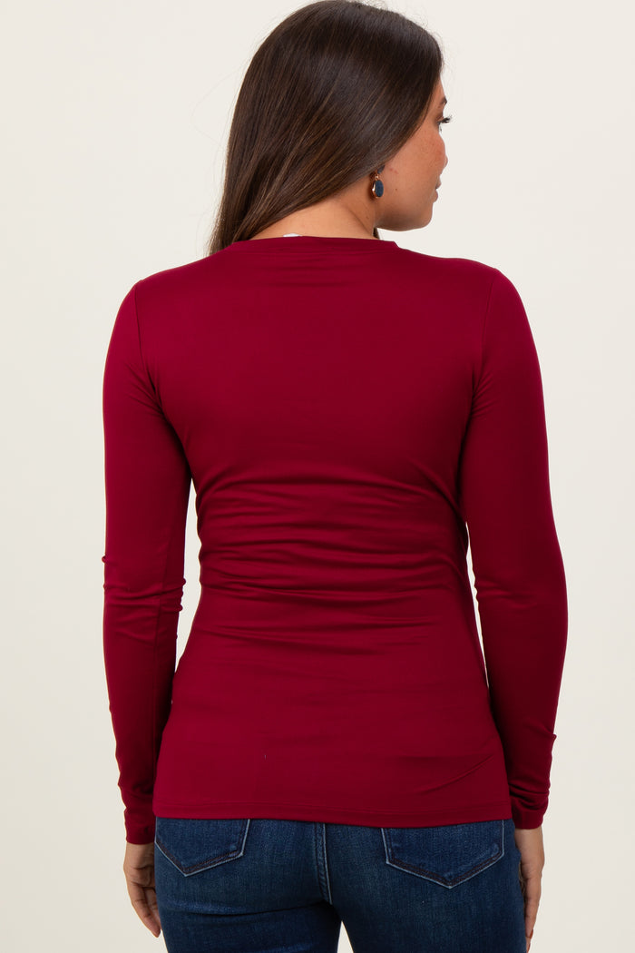 woman wearing a burgundy long sleeve maternity top, showing the back view and styled with fitted jeans