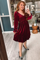 woman wearing a burgundy velvet dress with long sleeves and ruffled hem, posing in front of a mirror