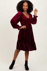 woman wearing a burgundy velvet smocked dress with long puff sleeves and a flared hem, posing with one hand on her hip
