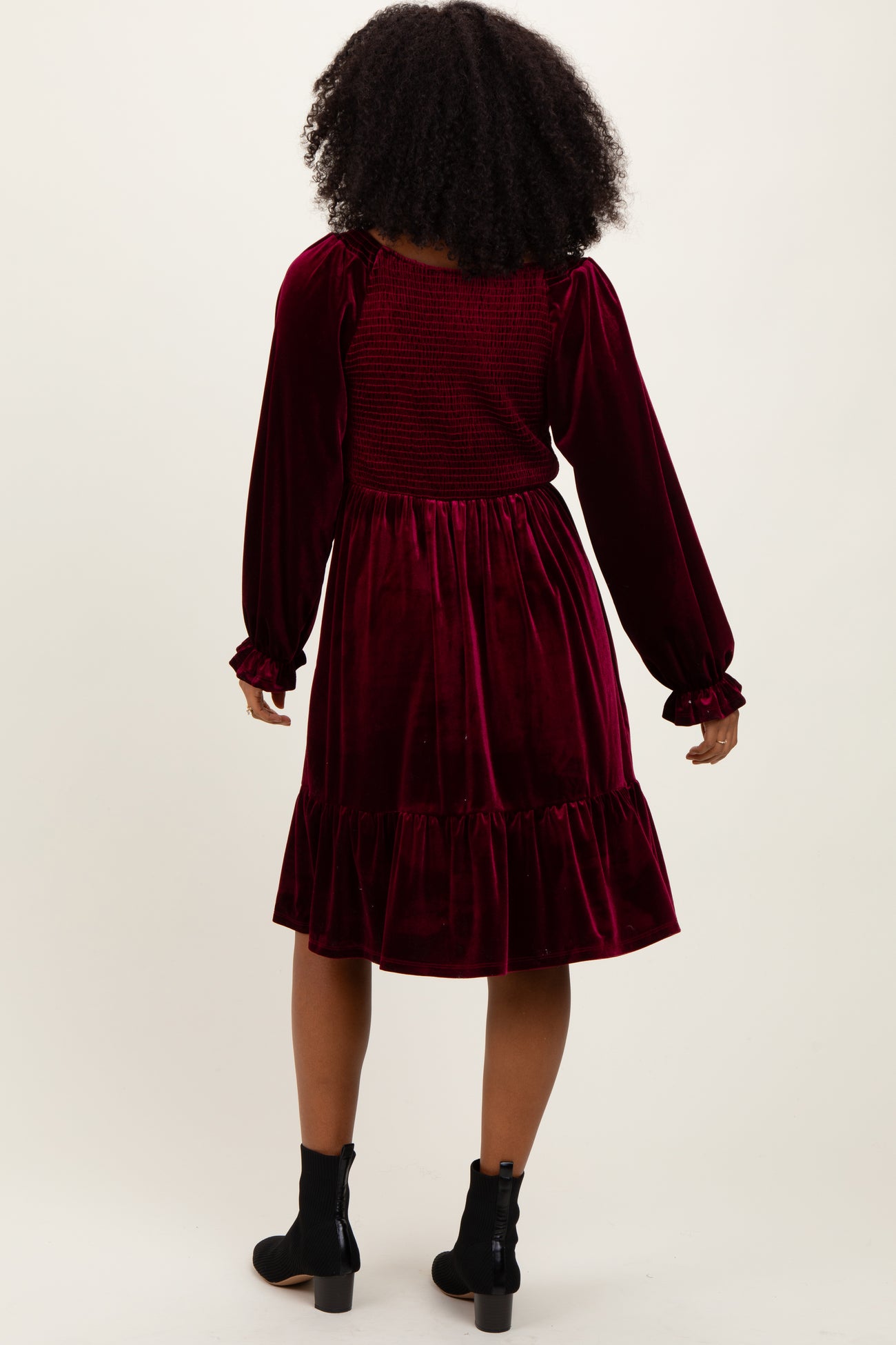 woman wearing a burgundy velvet dress with long sleeves and a ruffled hem, viewed from the back