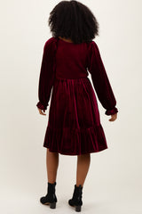 woman wearing a burgundy velvet dress with long sleeves and a ruffled hem, viewed from the back