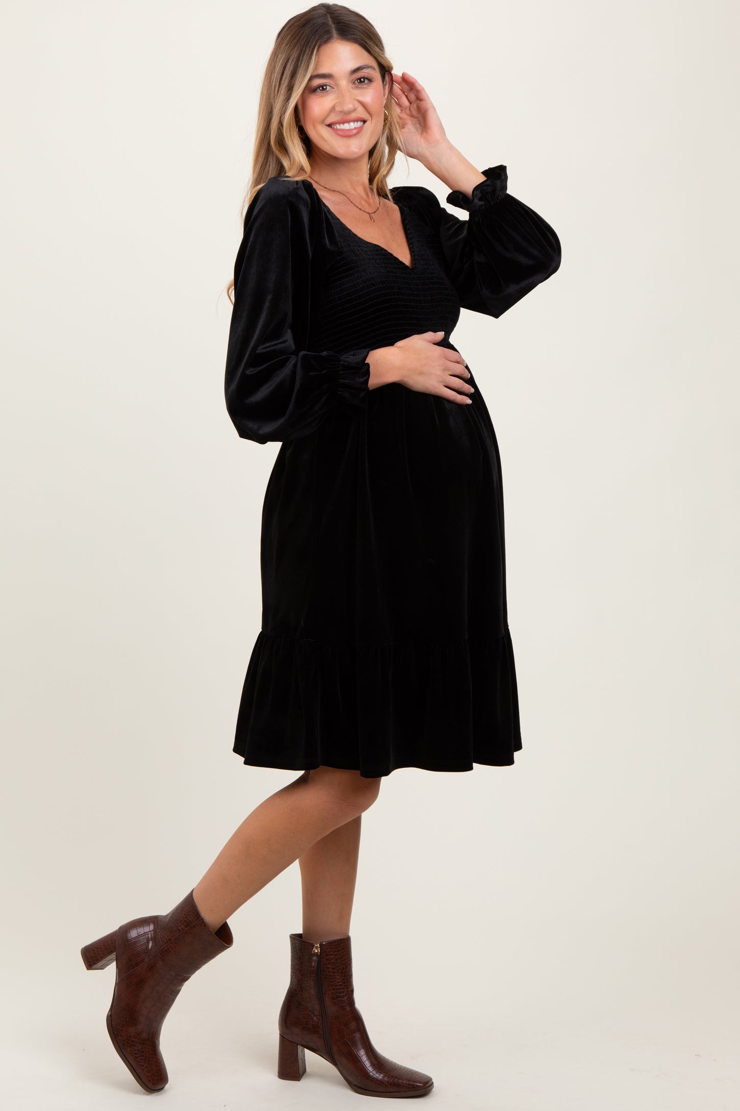 woman wearing a black velvet maternity dress with long puff sleeves and a ruffled hem, showing her baby bump
