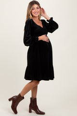 woman wearing a black velvet maternity dress with long puff sleeves and a ruffled hem, showing her baby bump