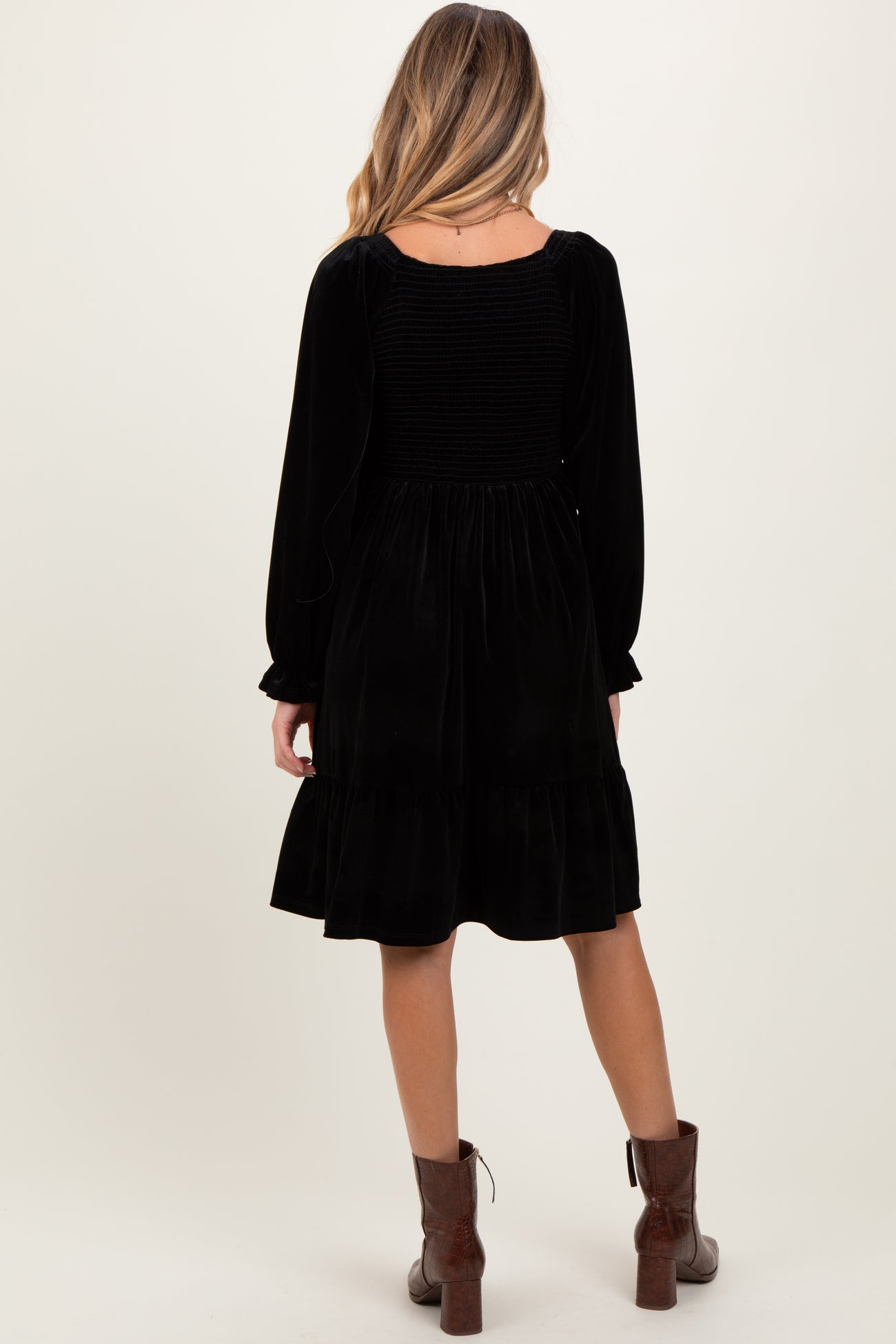 woman wearing a black velvet maternity dress with a smocked back and long sleeves, standing with her back to the camera