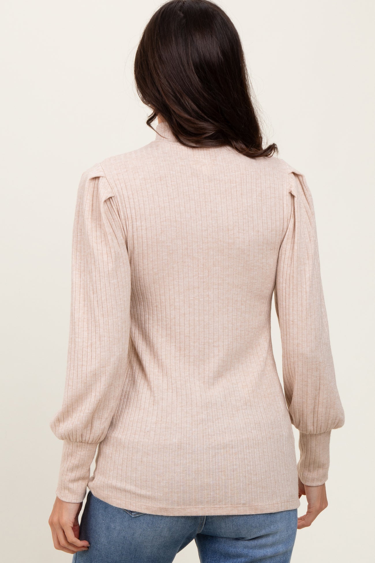 woman wearing a light beige ribbed sweater with puffed sleeves and a fitted silhouette, seen from the back