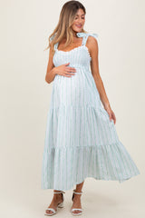 woman wearing a light blue and white striped maternity dress with ruffled tiers and bow straps, cradling her baby bump