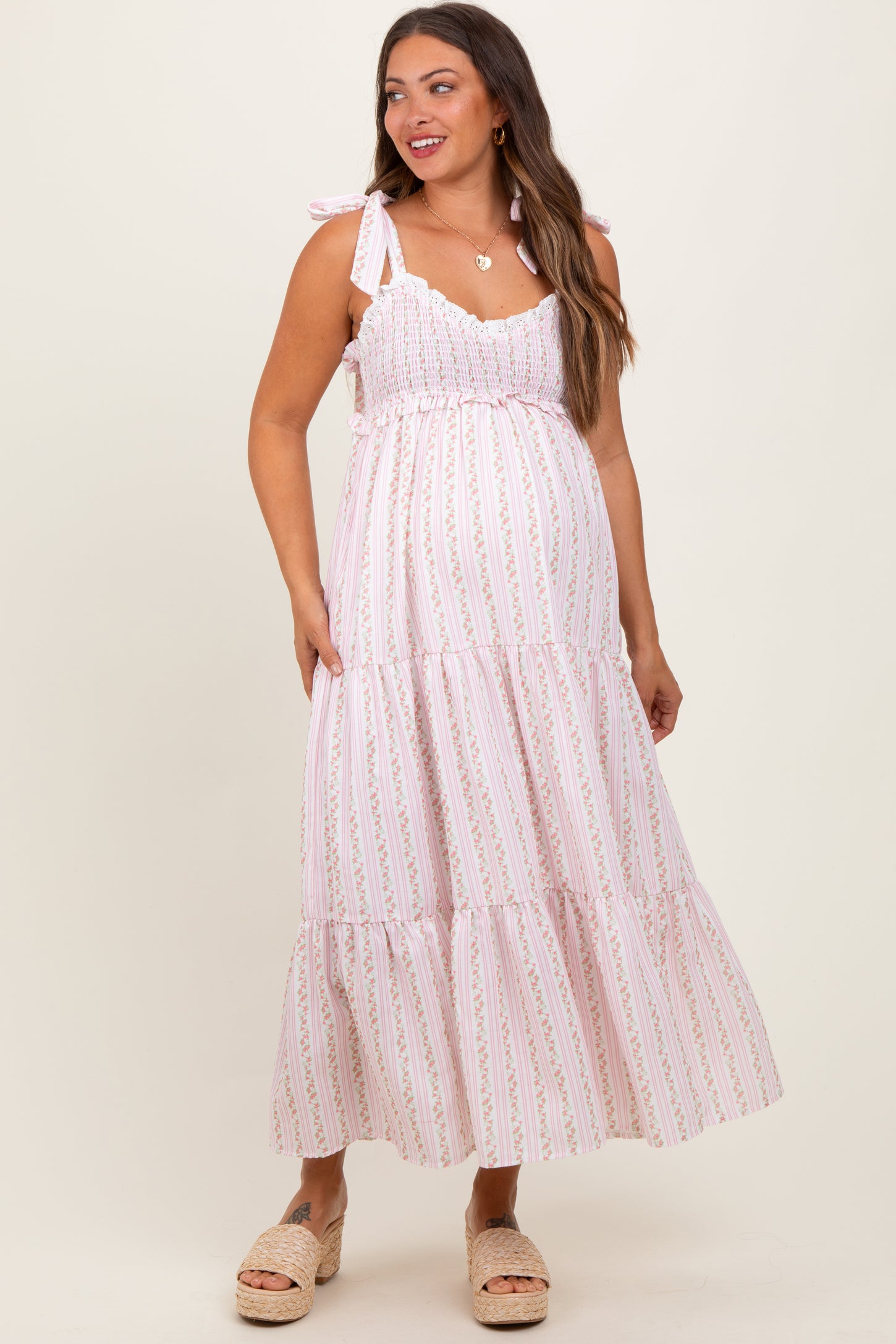 woman wearing a pink and white striped maternity maxi dress with tie straps and a visible baby bump