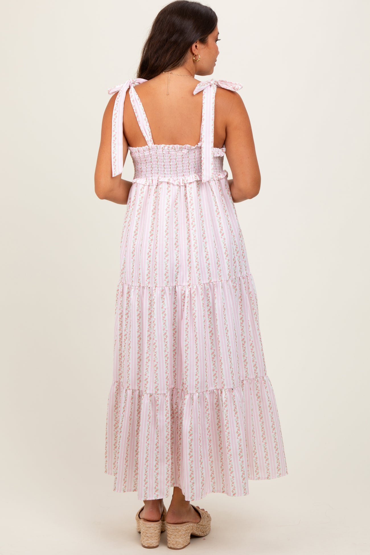 woman wearing a pink and white striped maternity maxi dress with tie straps and tiered ruffles, showing a baby bump