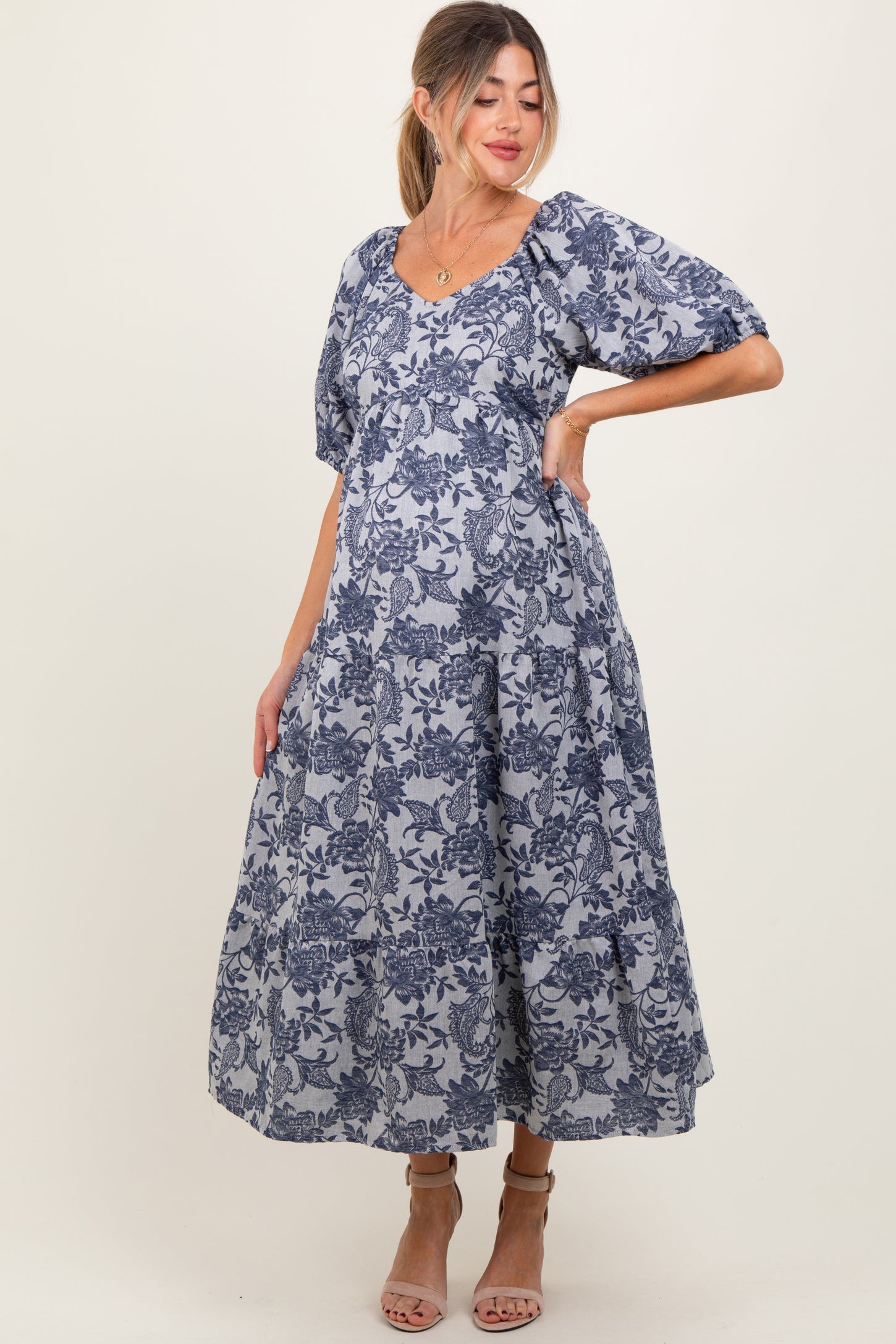 woman wearing a navy blue floral print maternity dress with puff sleeves and a flowing skirt, highlighting her baby bump