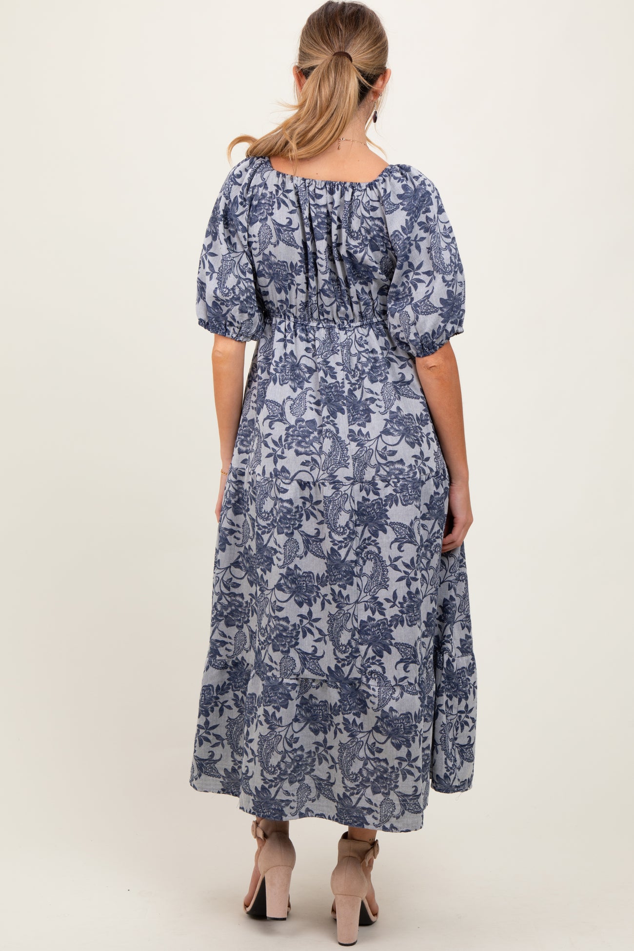woman wearing a blue floral maternity maxi dress with puff sleeves, showcasing a flowing fit and gathered back detail