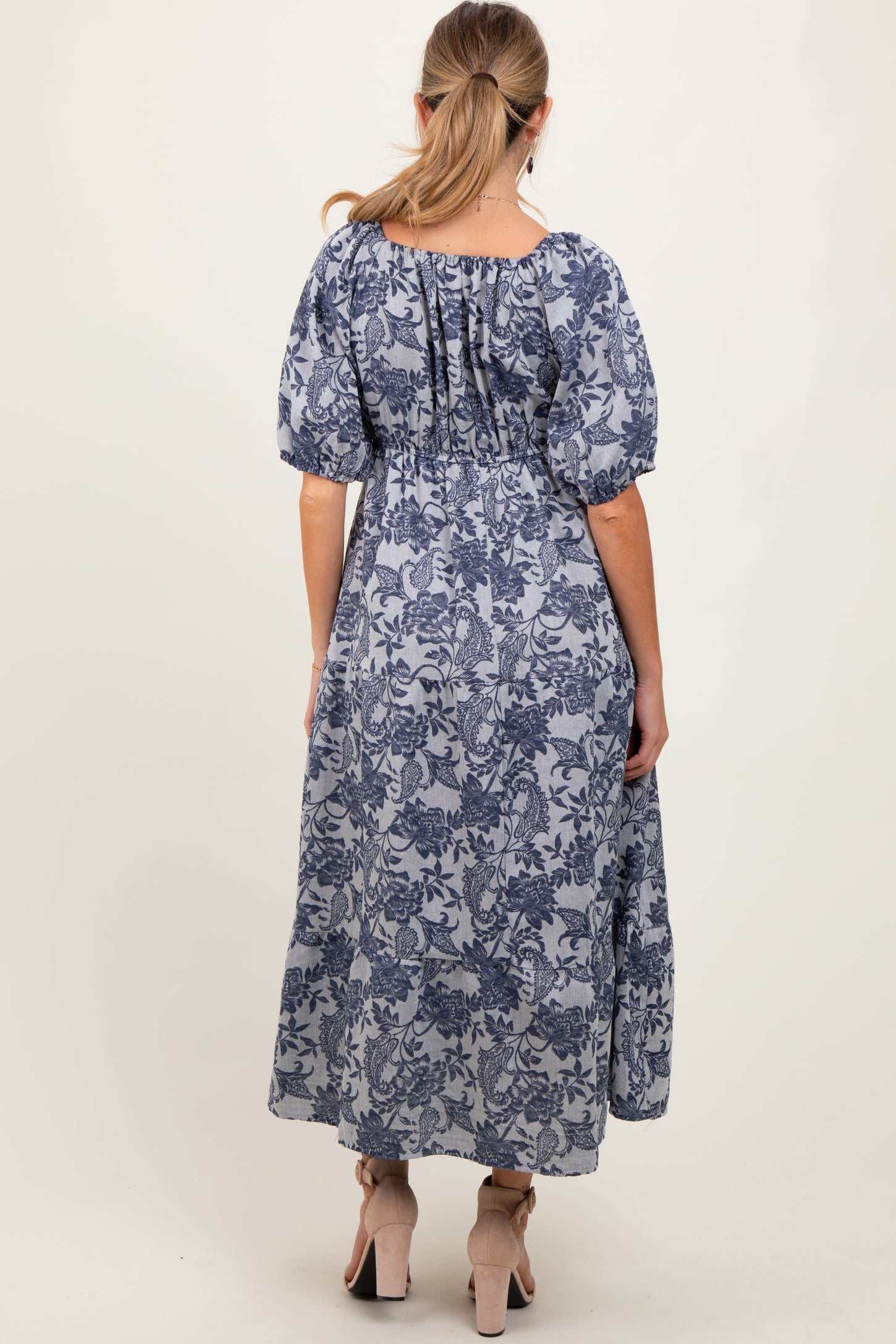 woman wearing a blue floral maternity maxi dress with puff sleeves, showcasing a flowing fit and gathered back detail