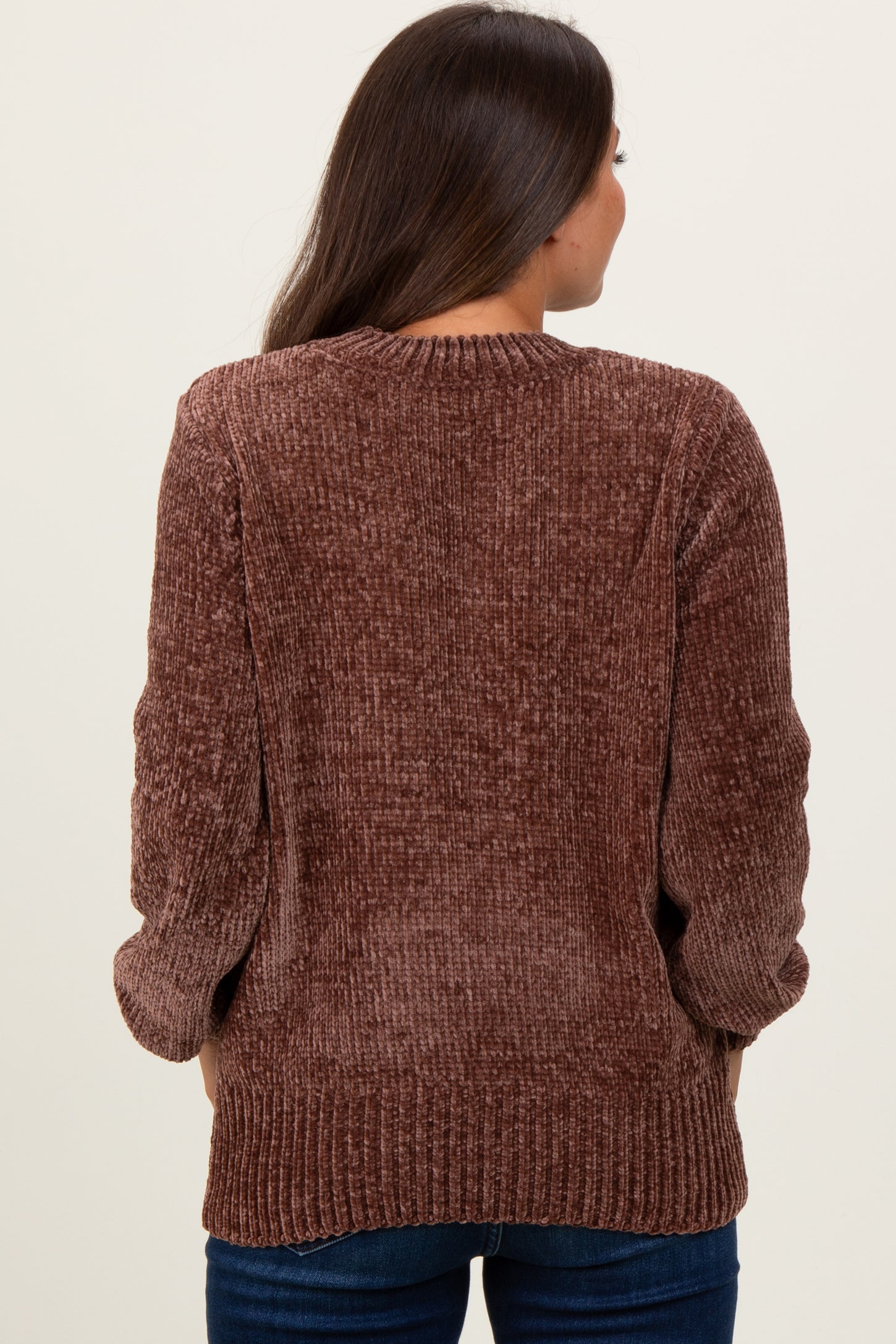 woman wearing a brown ribbed maternity sweater, seen from the back, paired with dark blue jeans