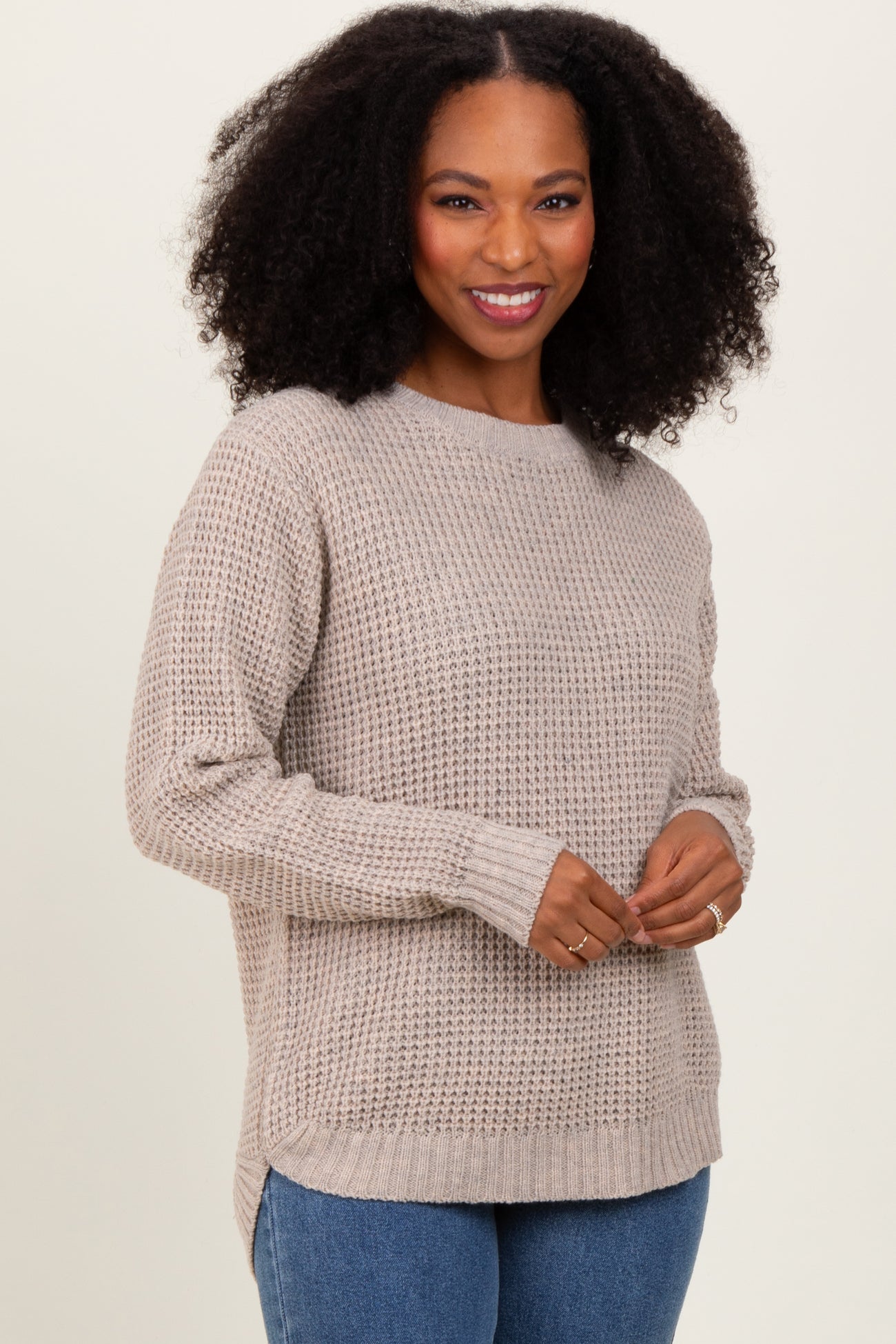 woman wearing a beige knit sweater with a relaxed fit and side slits, smiling at the camera