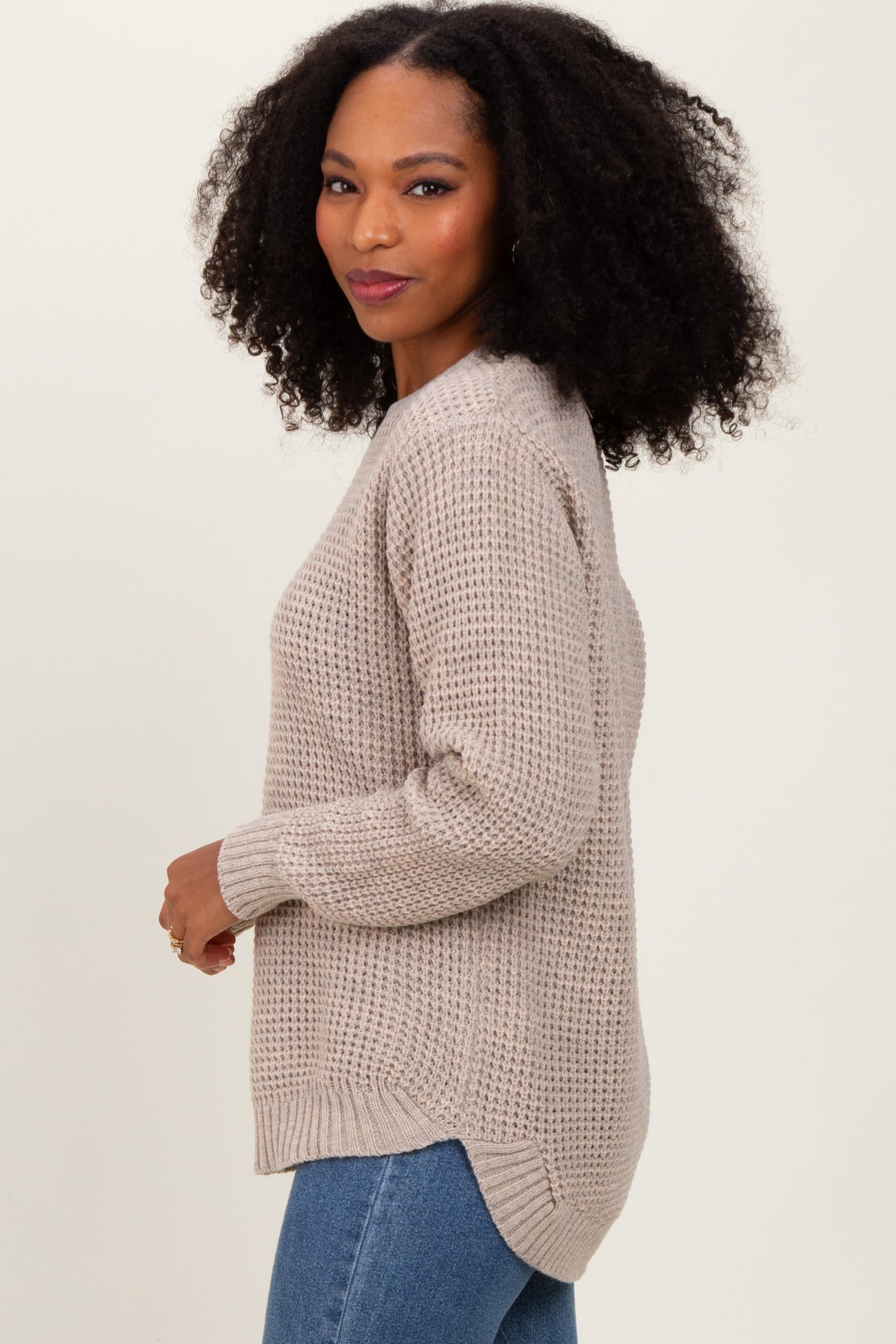 woman wearing a beige knit sweater with a relaxed fit and side slits, paired with blue jeans