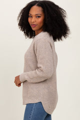 woman wearing a beige knit sweater with a relaxed fit and side slits, paired with blue jeans