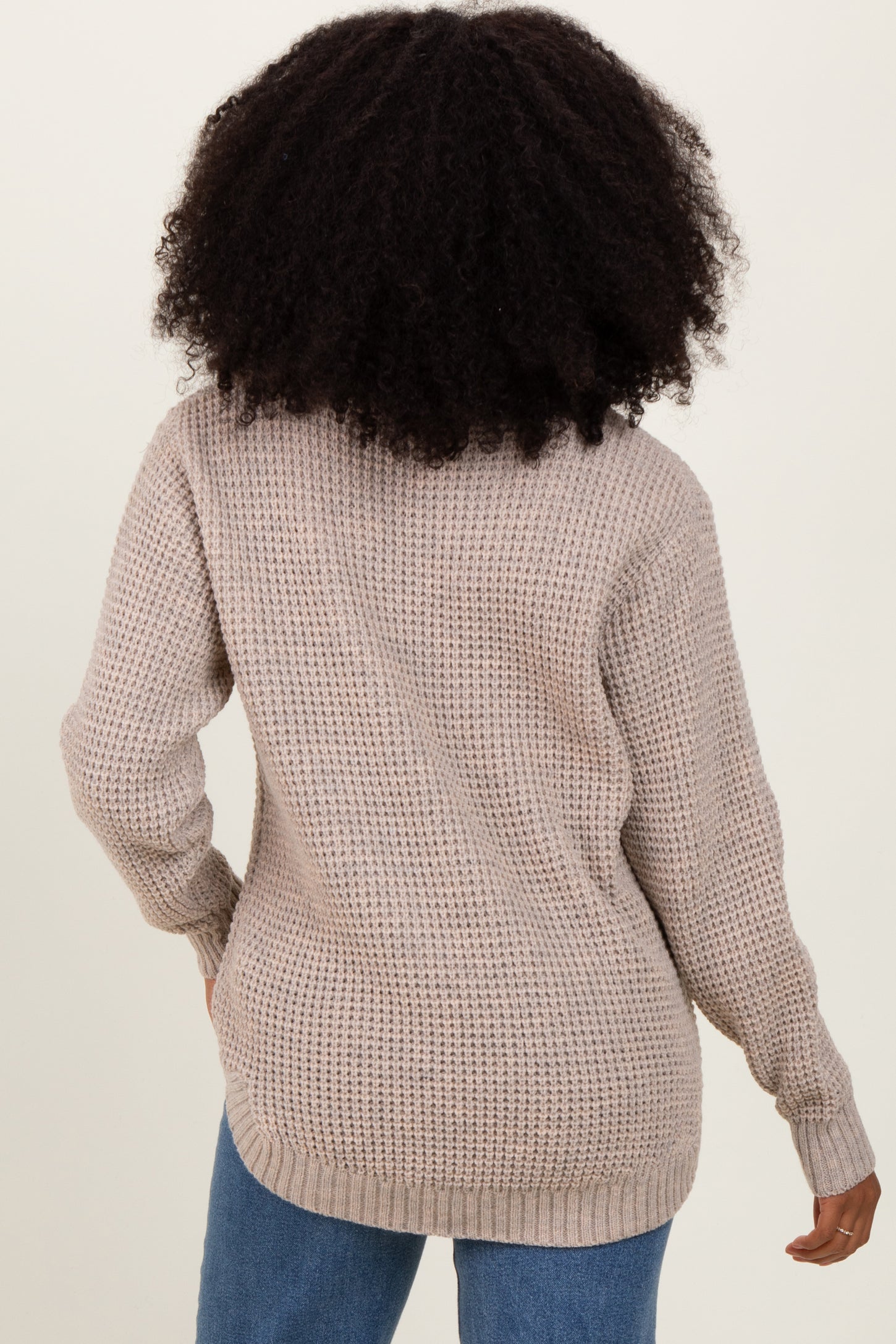 woman wearing a beige oversized knit sweater from the back, paired with light blue jeans