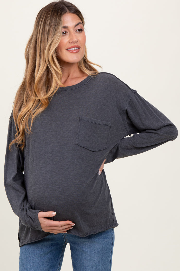 woman wearing a charcoal gray long sleeve maternity top, showing her baby bump while posing with one hand on her belly