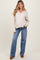 woman wearing a light beige ribbed maternity sweater with a v-neck and blue flared jeans, smiling with long wavy hair