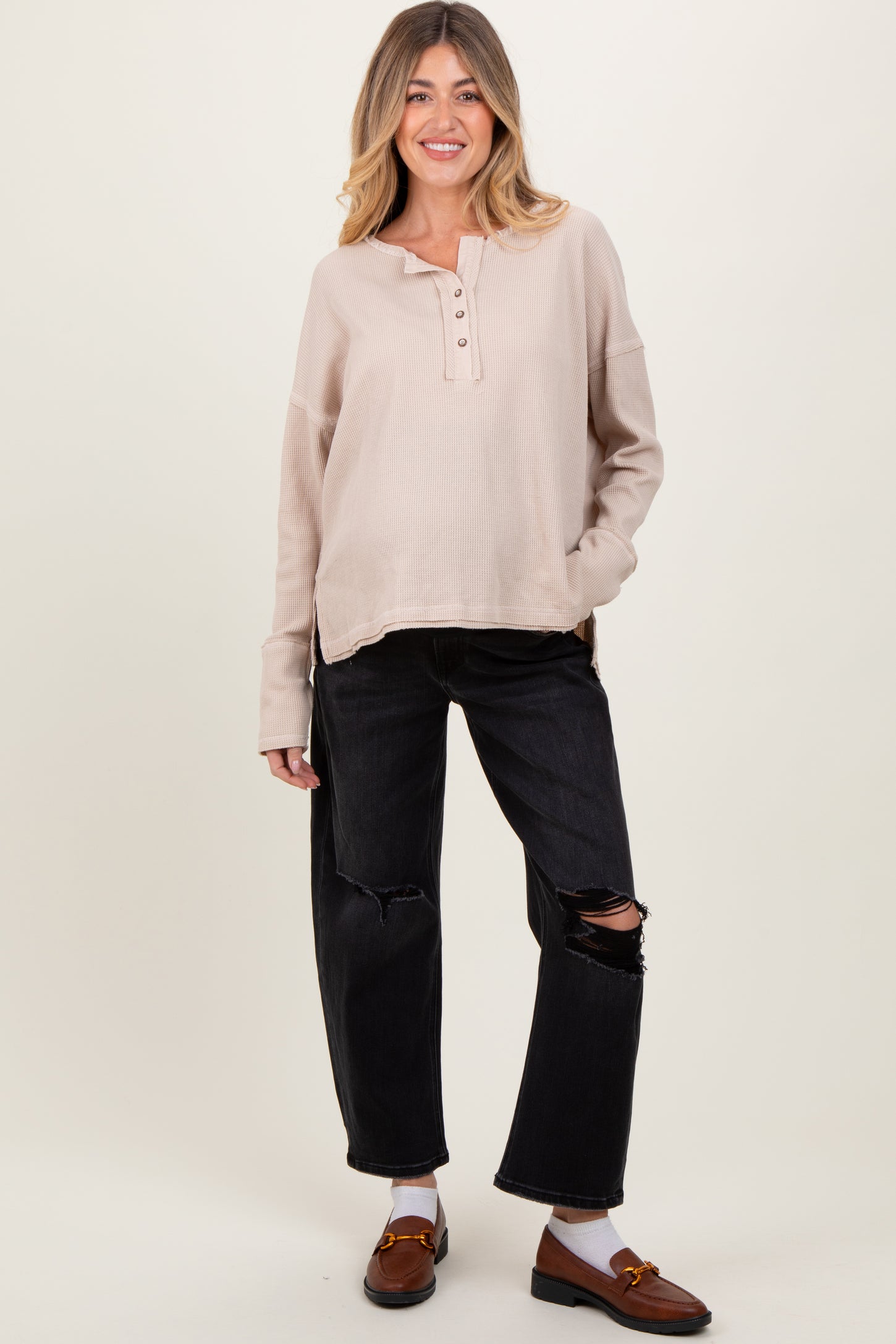 woman wearing a beige maternity long sleeve henley top with buttons and distressed black maternity jeans