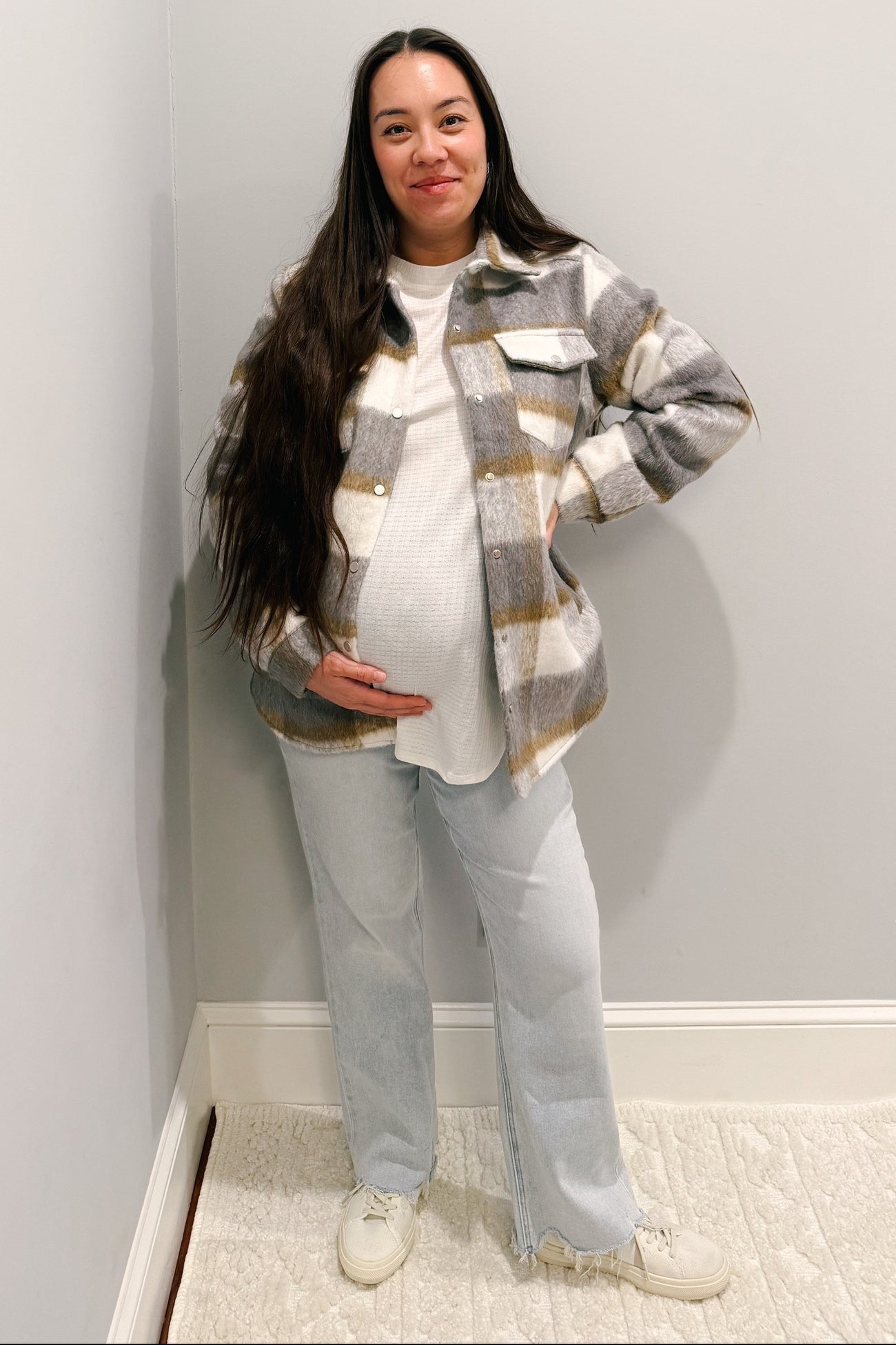 woman wearing a gray and white checkered maternity jacket over a white top with visible baby bump and light blue jeans