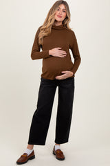woman wearing a brown long sleeve maternity top and holding her baby bump, paired with black wide-leg jeans