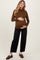 woman wearing a brown long sleeve maternity top and holding her baby bump, paired with black wide-leg jeans