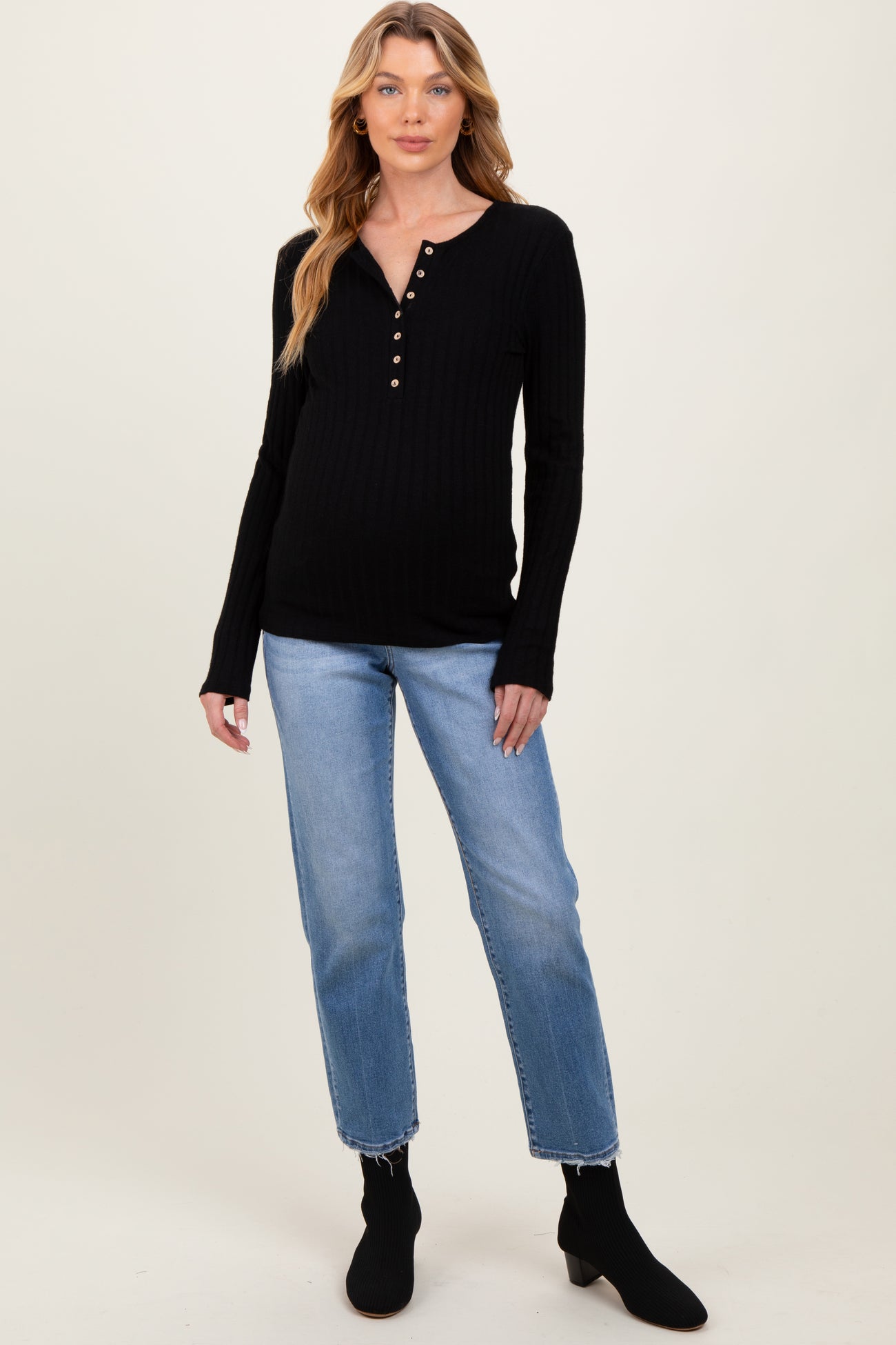 woman wearing a black ribbed maternity top with button details and blue jeans, showcasing a visible baby bump