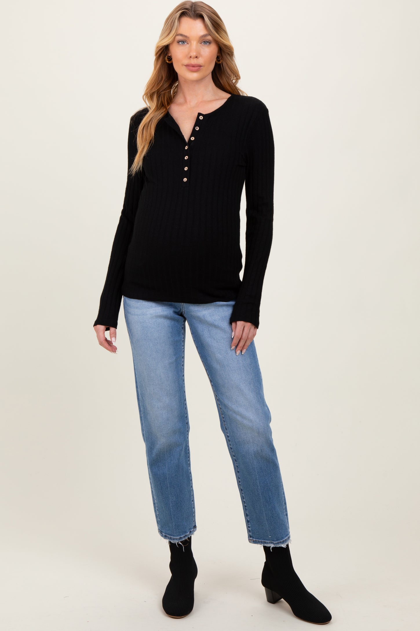 woman wearing a black ribbed maternity top with button details and blue jeans, showcasing a visible baby bump