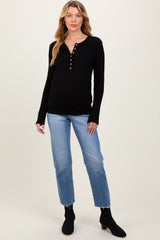 woman wearing a black ribbed maternity top with button details and blue jeans, showcasing a visible baby bump