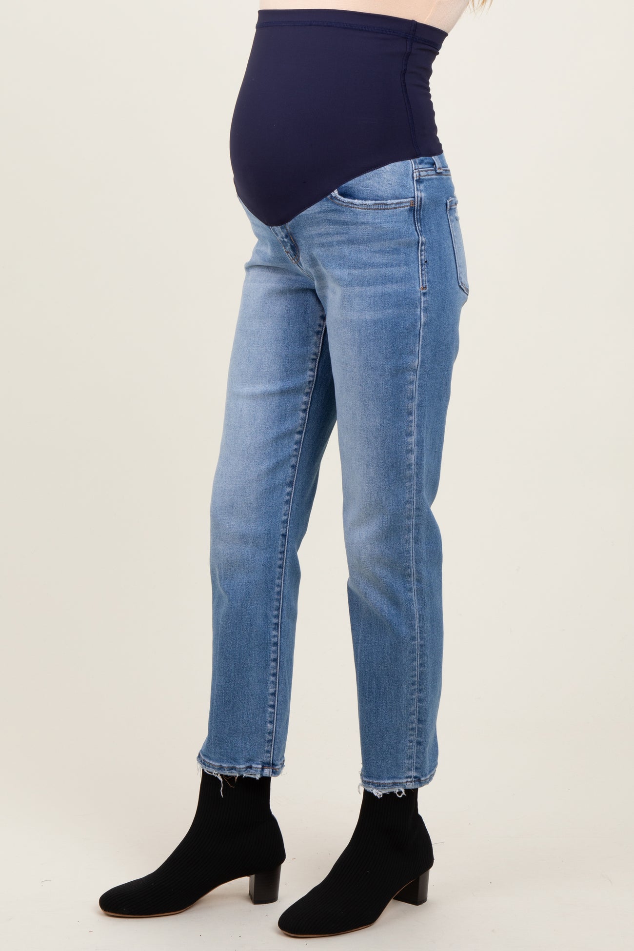 woman wearing light blue maternity jeans with a dark blue waistband and a visible baby bump