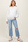 woman wearing a white knitted hoodie and light blue ripped jeans, showcasing her baby bump in maternity wear