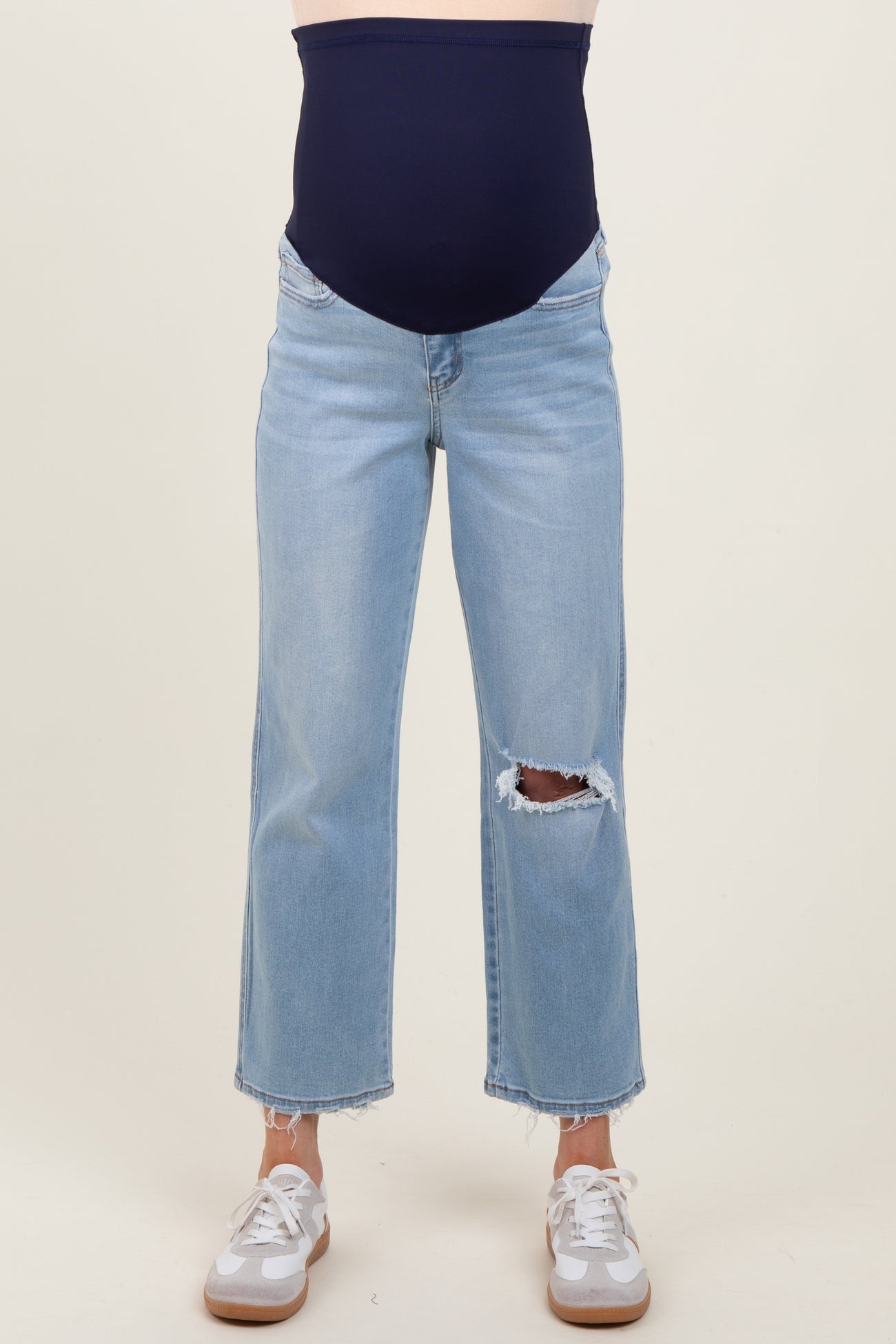 woman wearing light blue distressed maternity jeans with a navy blue belly panel and white sneakers