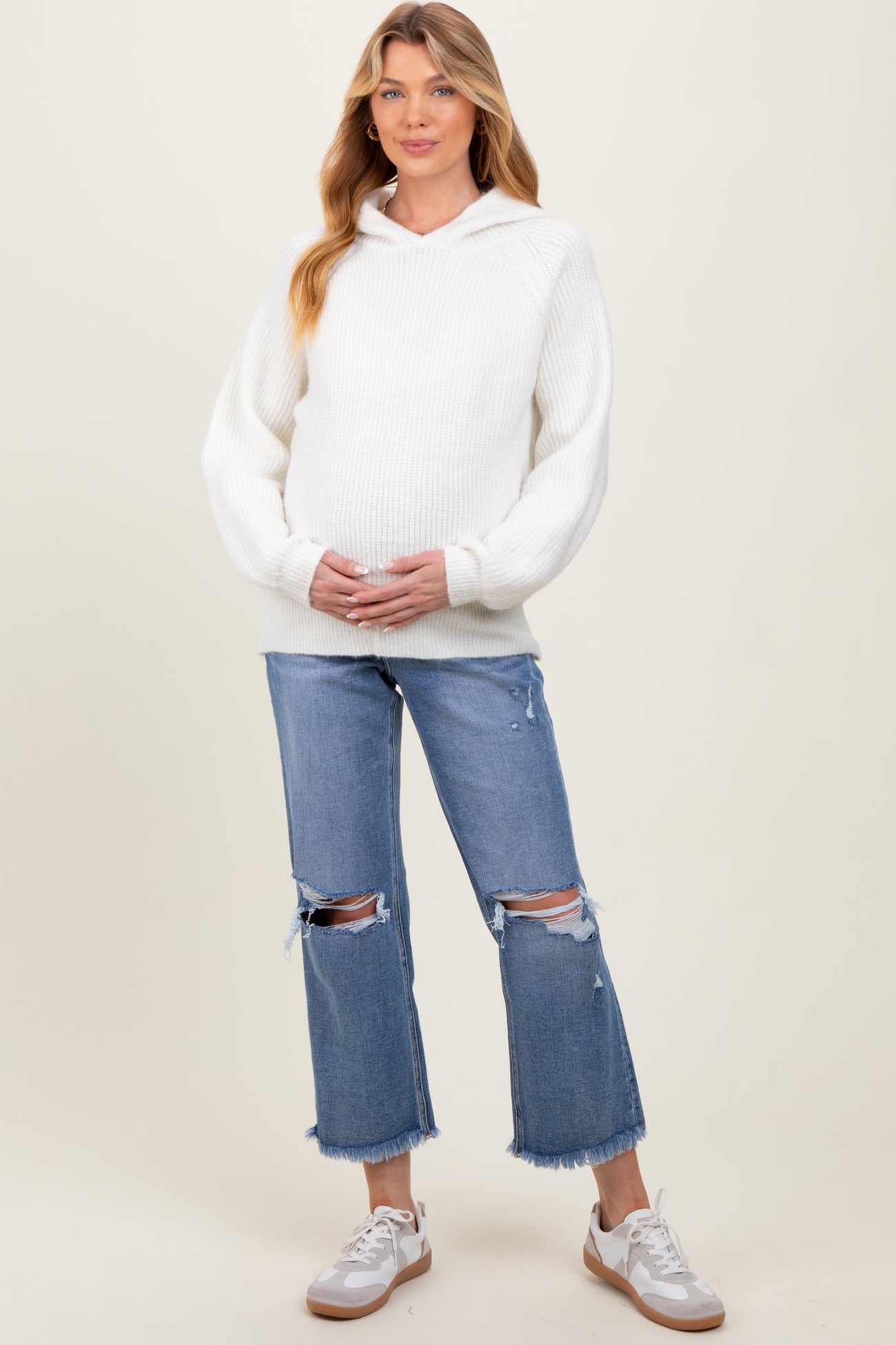 woman wearing a white ribbed maternity hoodie and distressed light wash jeans, holding her baby bump