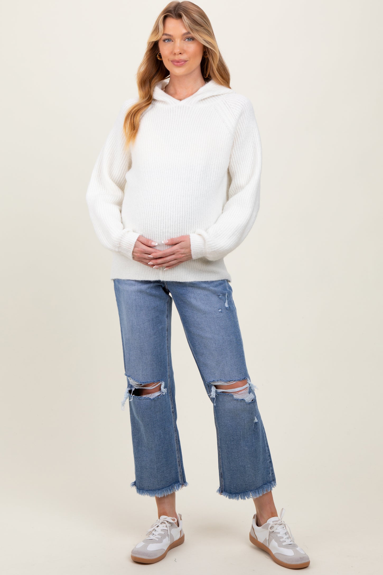 woman wearing a white ribbed maternity hoodie and distressed light wash jeans, holding her baby bump