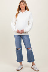 woman wearing a white ribbed maternity hoodie and distressed light wash jeans, holding her baby bump