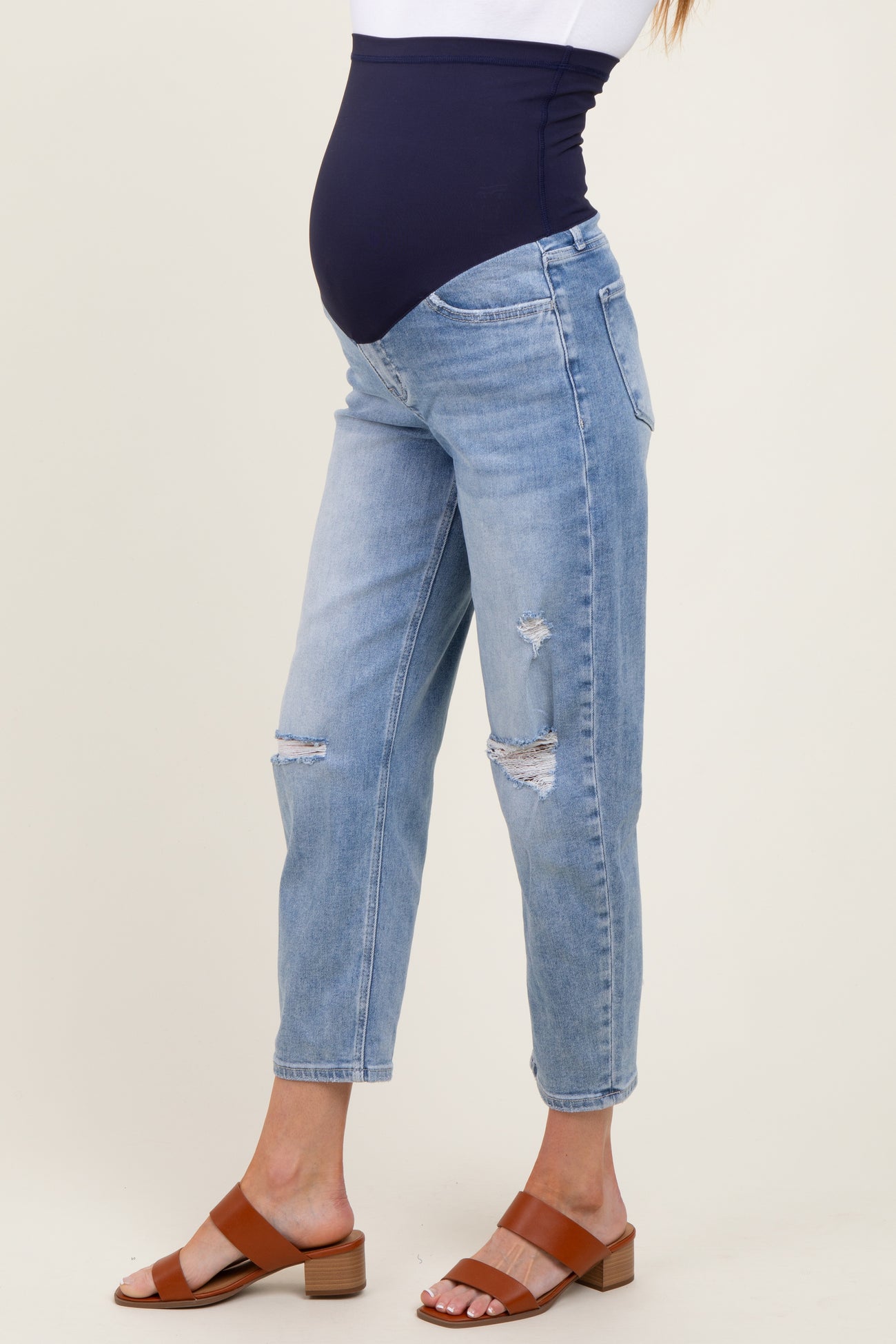 woman wearing light blue distressed maternity jeans with a navy belly band and brown block-heeled sandals